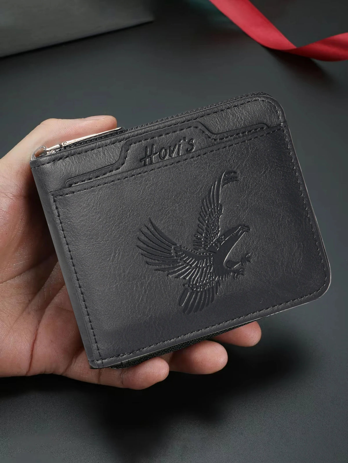 A dark gray embossed PU leather slim wallet with a bird design is held in a hand.