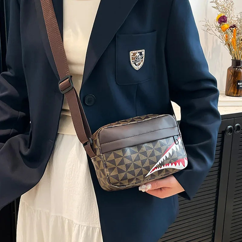 A dark blue blazer is shown holding a brown and tan patterned square crossbody purse with a silver emblem.