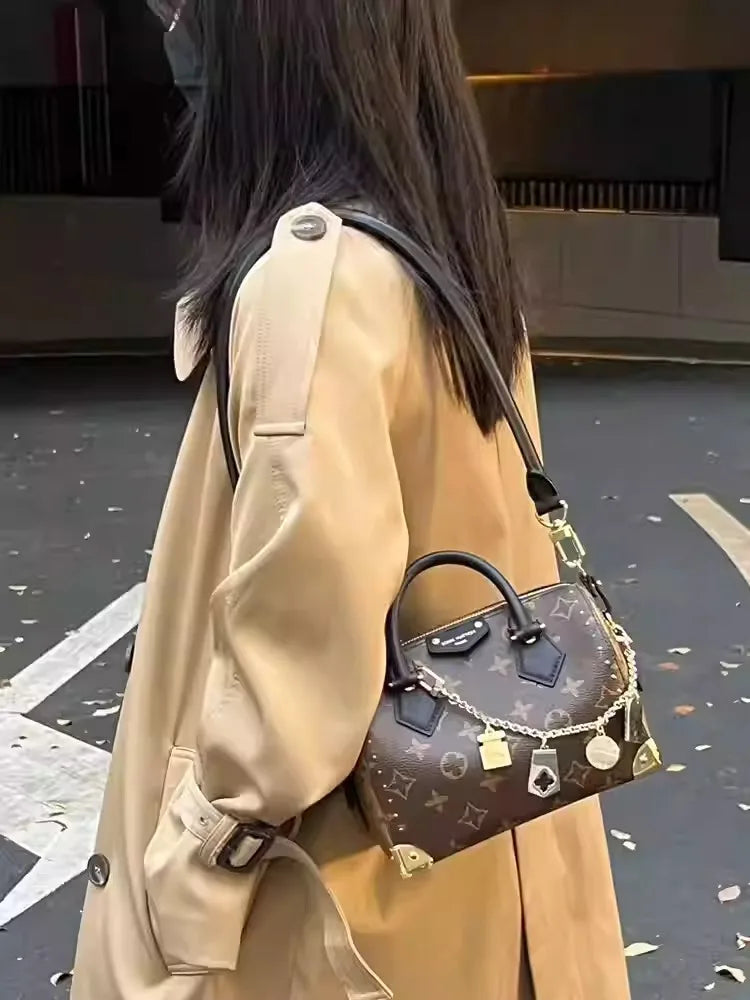A person is wearing a tan leather coat and carrying a dark brown cowhide leather bag with a gold chain strap.