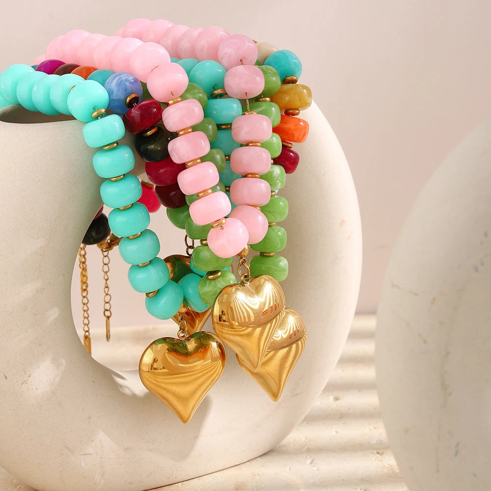 A colorful bead necklace featuring pink, blue, and green resin heart charms displayed on a white ceramic surface.