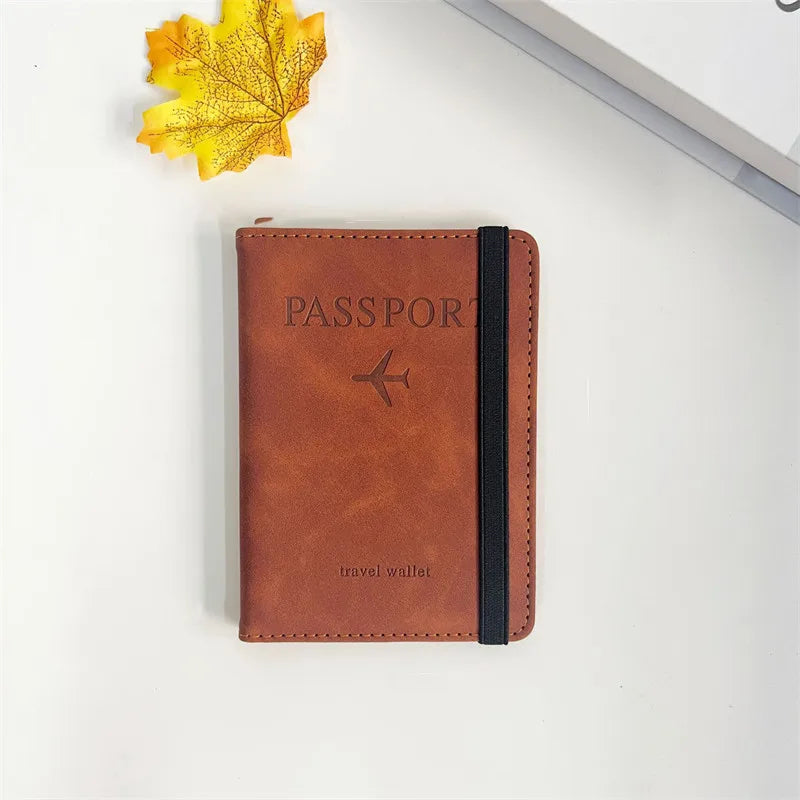 A brown leather passport wallet with a black sleeve rests on a white surface next to a yellow autumn leaf.