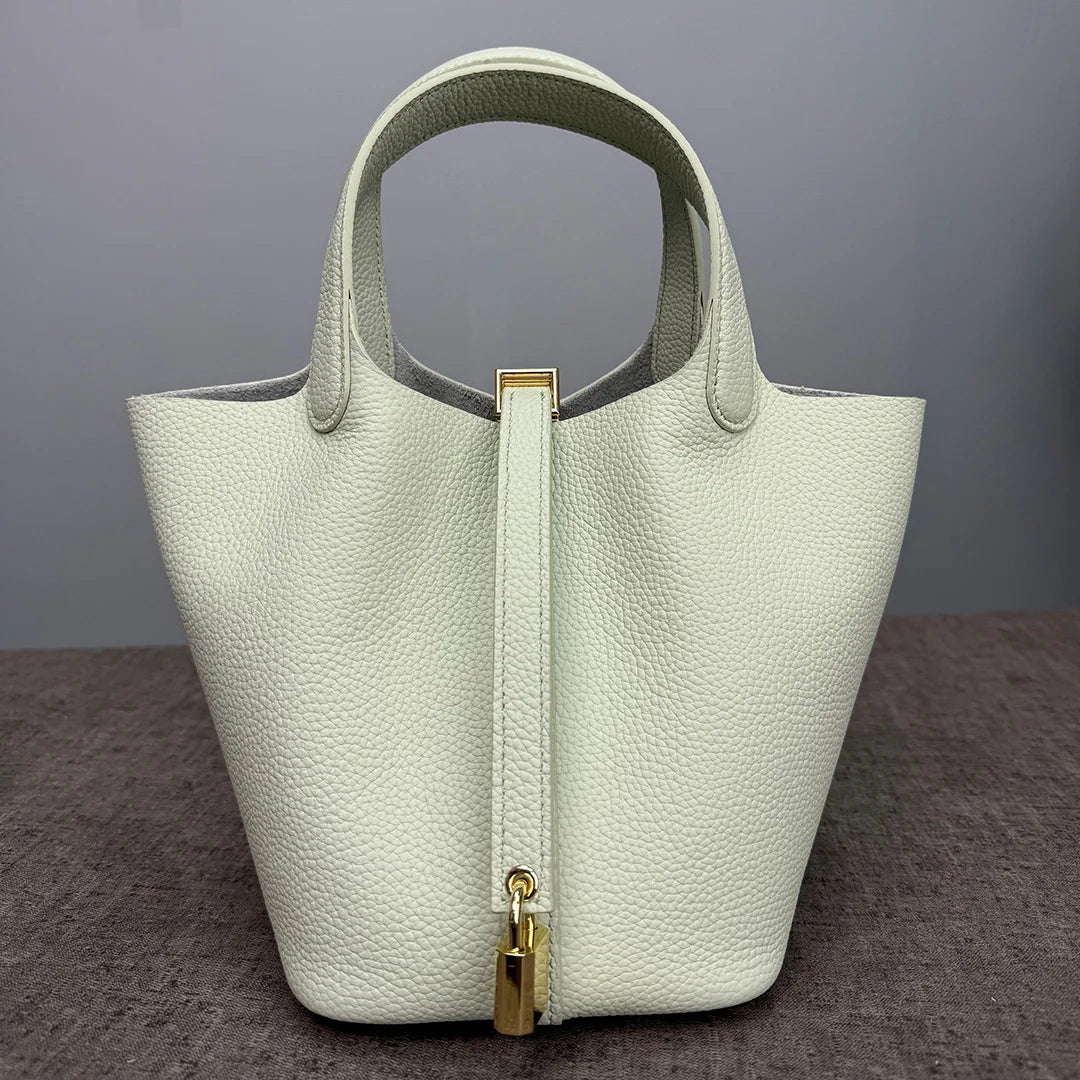 A light cream leather bucket bag with a vertical zipper closure and gold hardware.