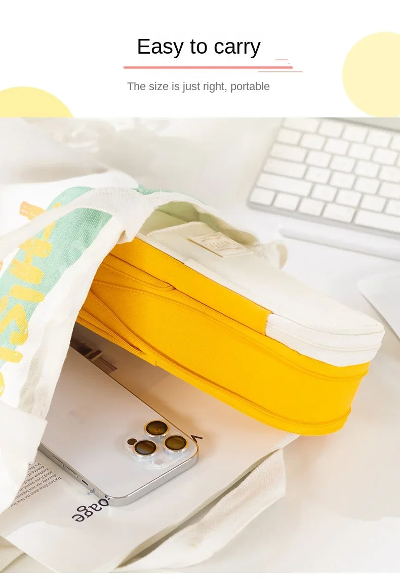 Une trousse à crayons en toile jaune ouverte, avec un smartphone posé à l'intérieur sur une surface blanche.
