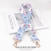 A light blue and purple floral patterned fabric strap with gold hardware displayed on a white background.