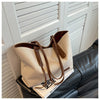 A beige canvas shoulder tote bag with brown leather accents resting on a black leather sofa.