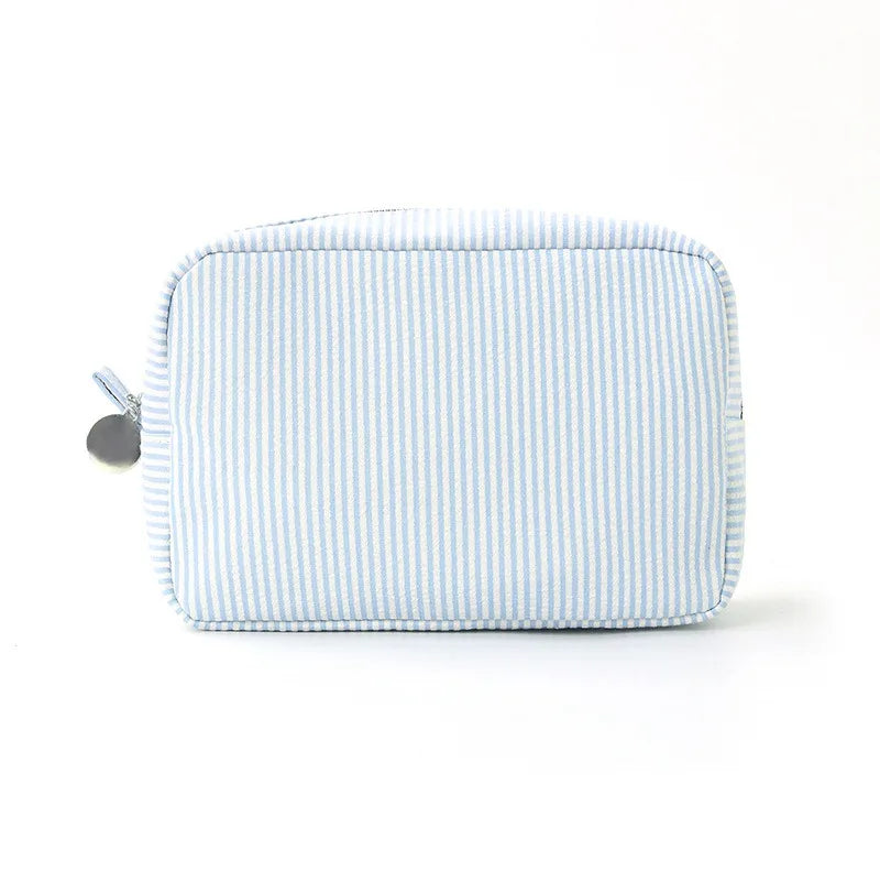 A light blue and white striped seersucker cosmetic bag with a zipper closure.