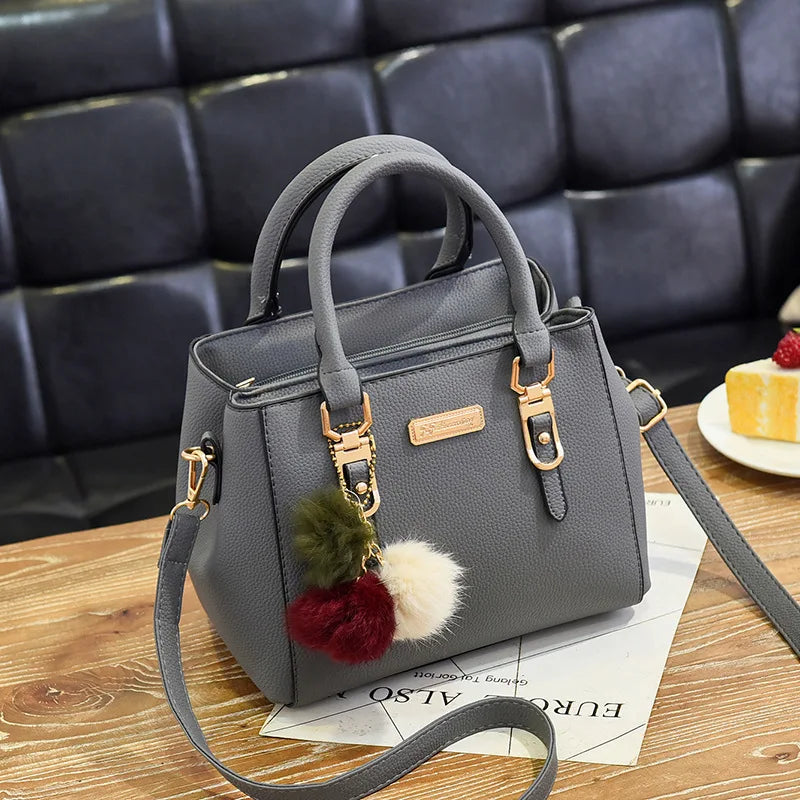 A gray vintage PU leather tassel handbag resting on a wooden surface.