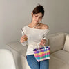 A woman holds a colorful hand woven PVC vegetable basket tote bag while sitting on a sofa.