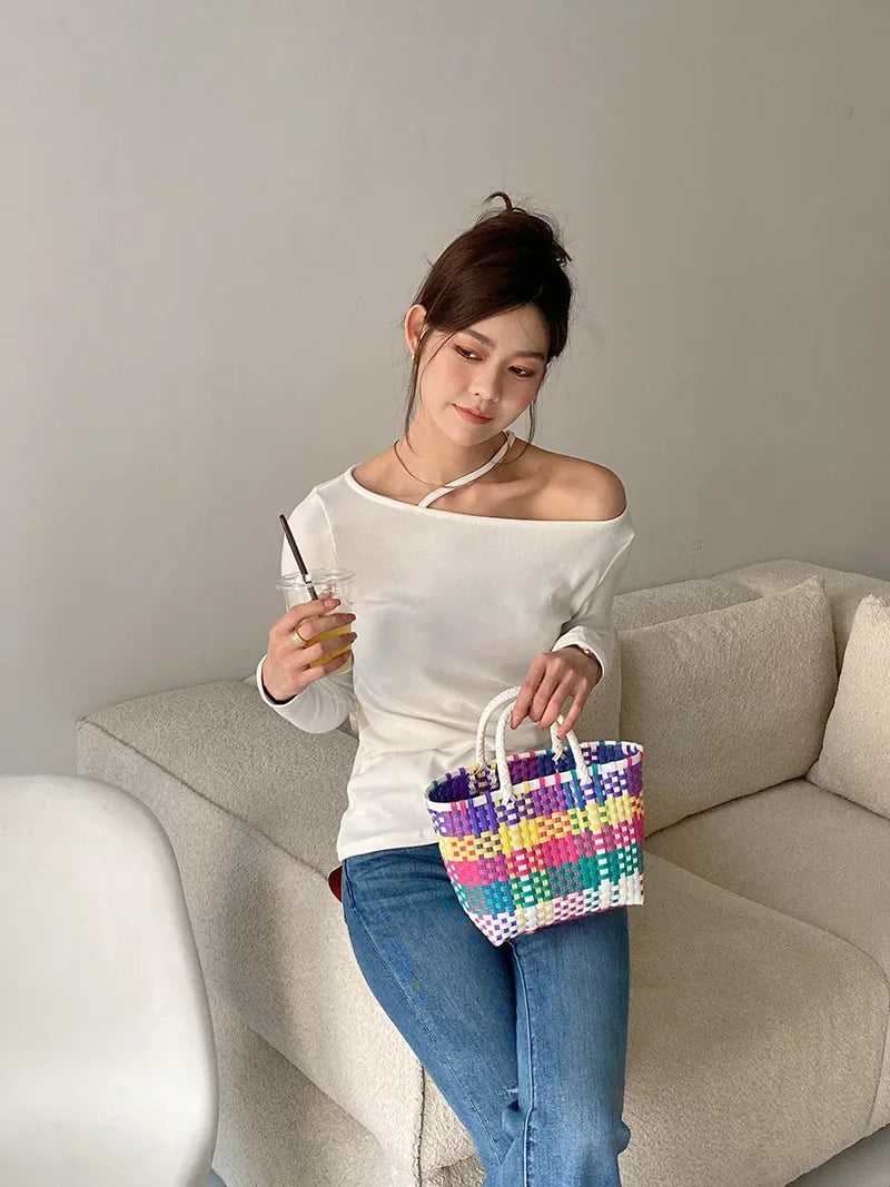 A woman holds a colorful hand woven PVC vegetable basket tote bag while sitting on a sofa.