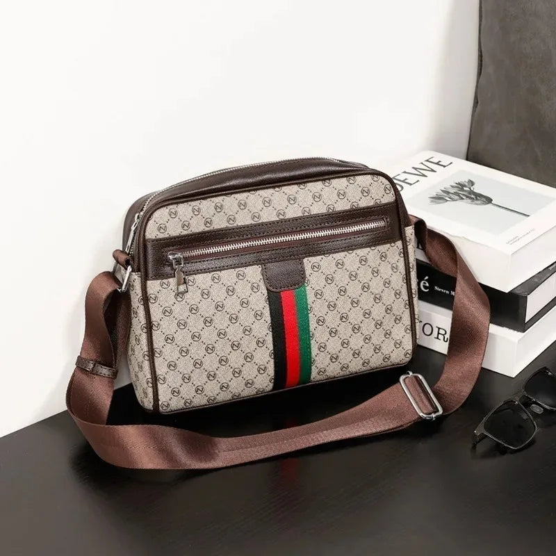 A brown men's letter print crossbody sling bag resting on a dark surface next to a white box.