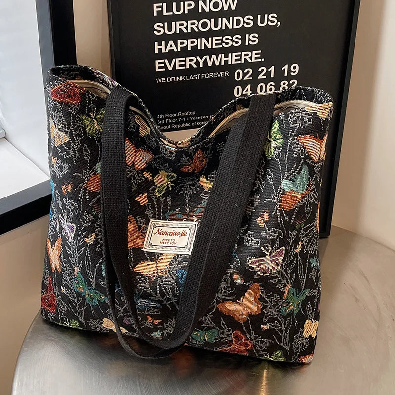 A black and orange bohemian corduroy tote bag with floral embroidery displayed in front of a framed sign.