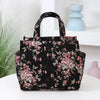 A floral patterned black cloth tote bag with pink and green leaves sitting on a white surface.