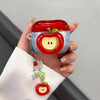 A hand holds a red apple shaped earphone case with blue accents and a silver charm.