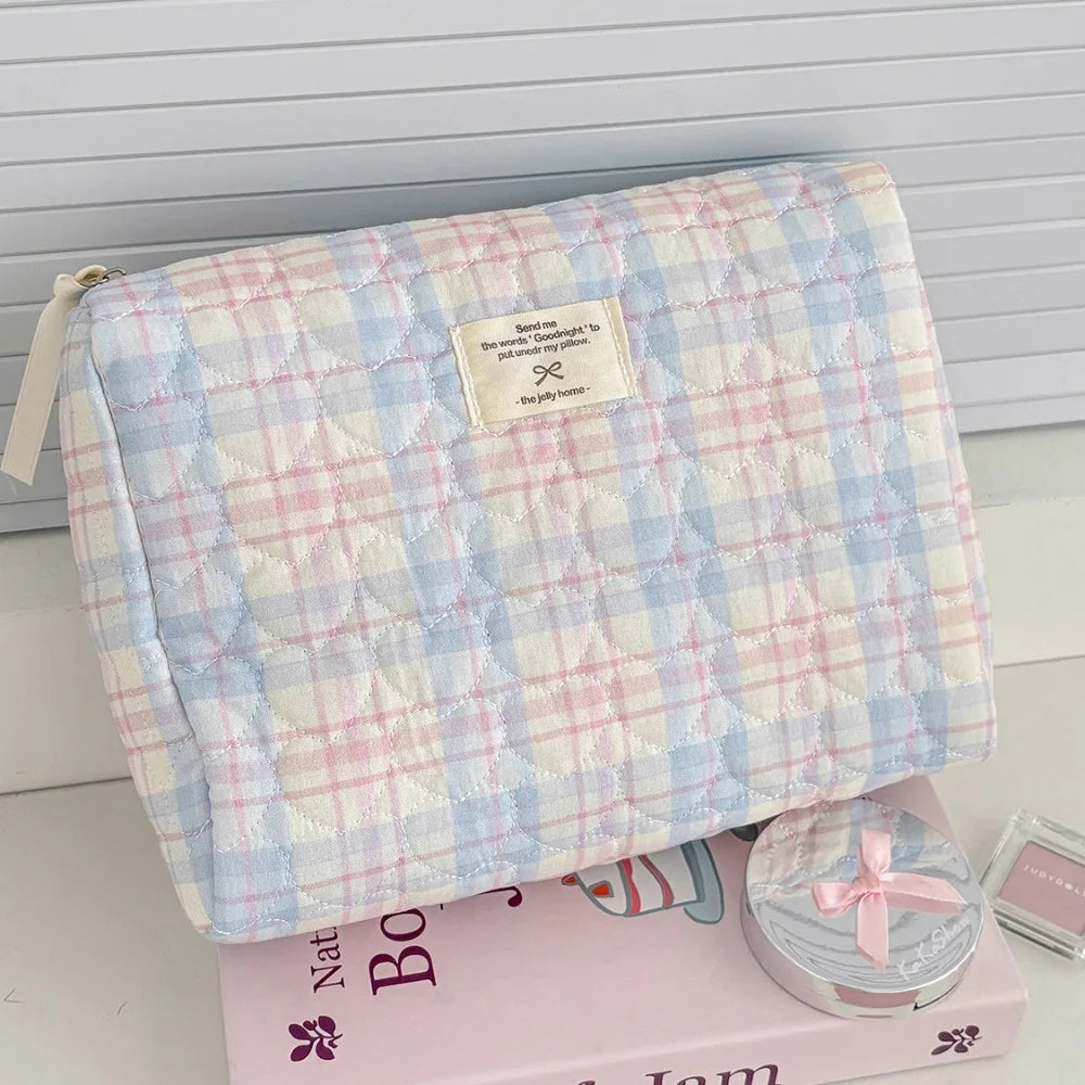 A light blue and pink plaid quilted cosmetic bag with a white label resting on a pink box.