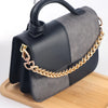 A black and gray heart-shaped purse with a gold chain extender resting on a wooden surface.