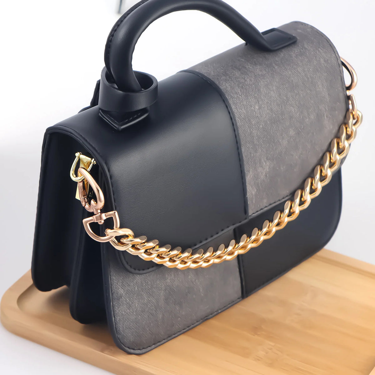 A black and gray heart-shaped purse with a gold chain extender resting on a wooden surface.