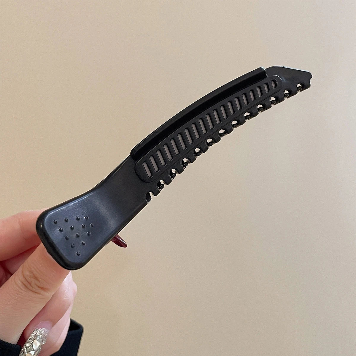 Une main tient une pince à cheveux noire professionnelle antidérapante avec des bords dentelés et de petites pointes.