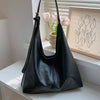 A black PU leather slouchy hobo shoulder bag is displayed on a white shelf next to pink tulips.