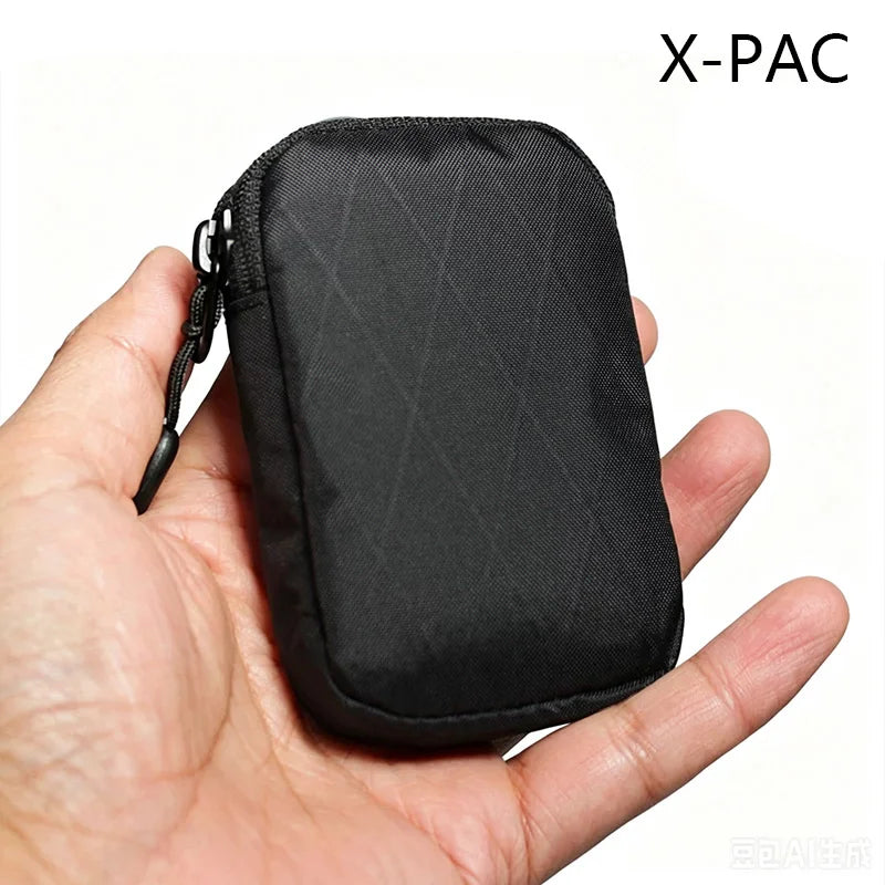 Une pochette utilitaire noire X-PAC pour clés et essentiels tenue dans une main.