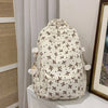 Mochila de color crema con estampado floral negro y múltiples bolsillos, exhibida sobre una superficie blanca.