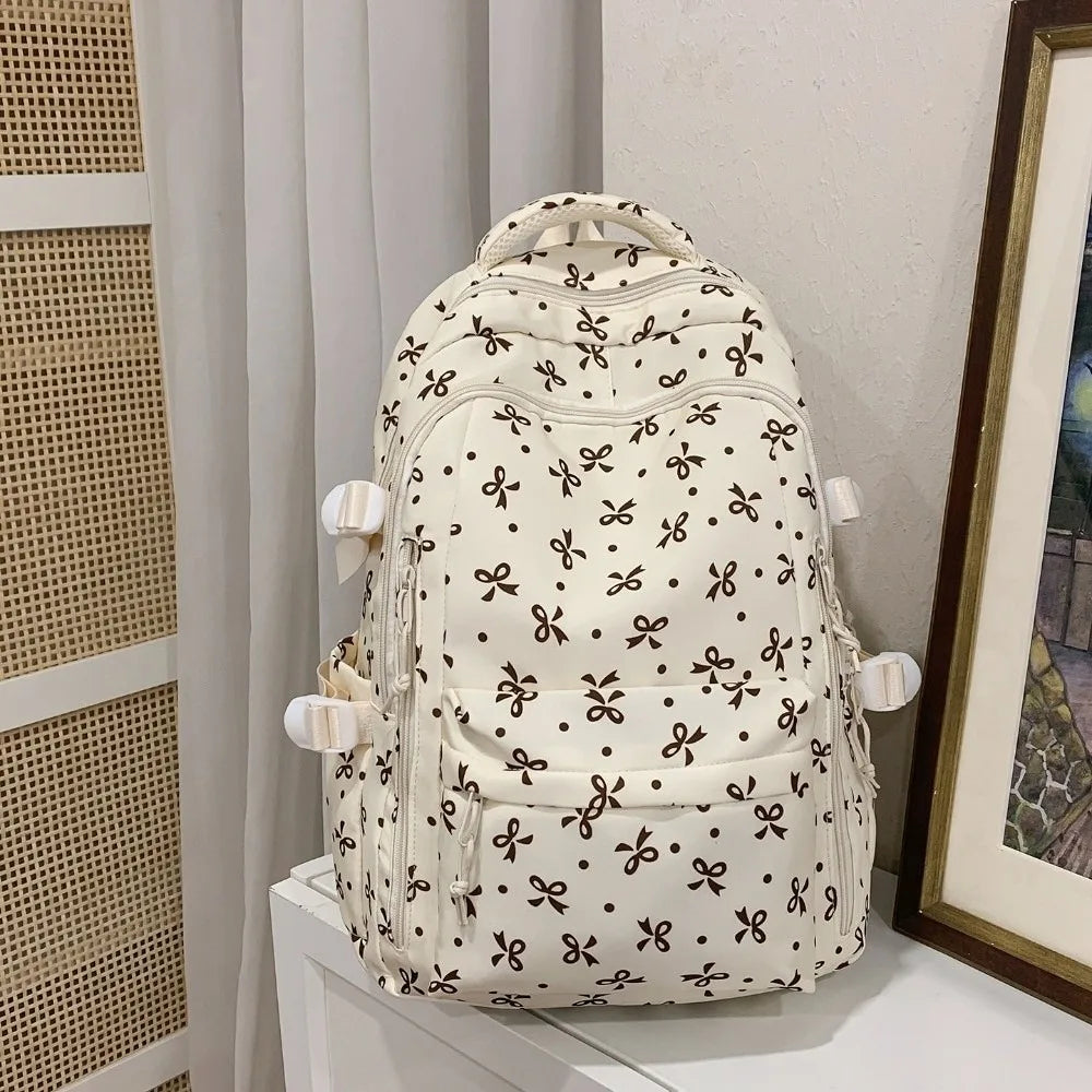 Mochila de color crema con estampado floral negro y múltiples bolsillos, exhibida sobre una superficie blanca.