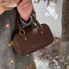 A brown vintage PU leather shoulder bag carried by a person wearing a gray sweater and plaid skirt.