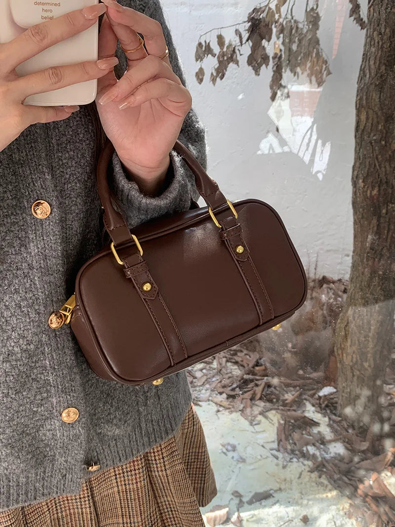 A brown vintage PU leather shoulder bag carried by a person wearing a gray sweater and plaid skirt.