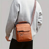Sac bandoulière en cuir marron porté par une personne, avec un pull gris et une sangle beige.