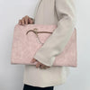 A woman holds a pale pink slim PU laptop sleeve in front of her white blazer.