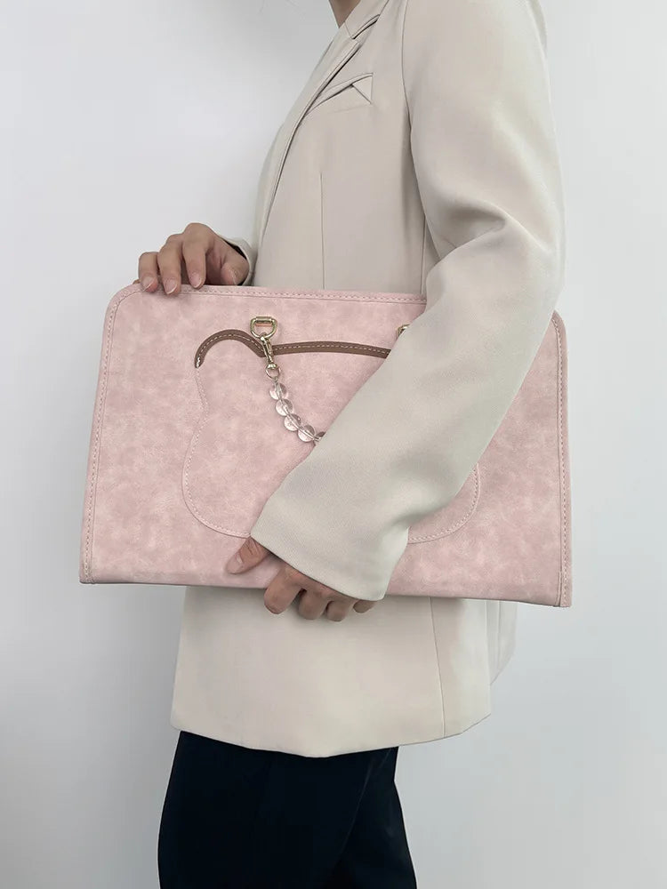 A woman holds a pale pink slim PU laptop sleeve in front of her white blazer.