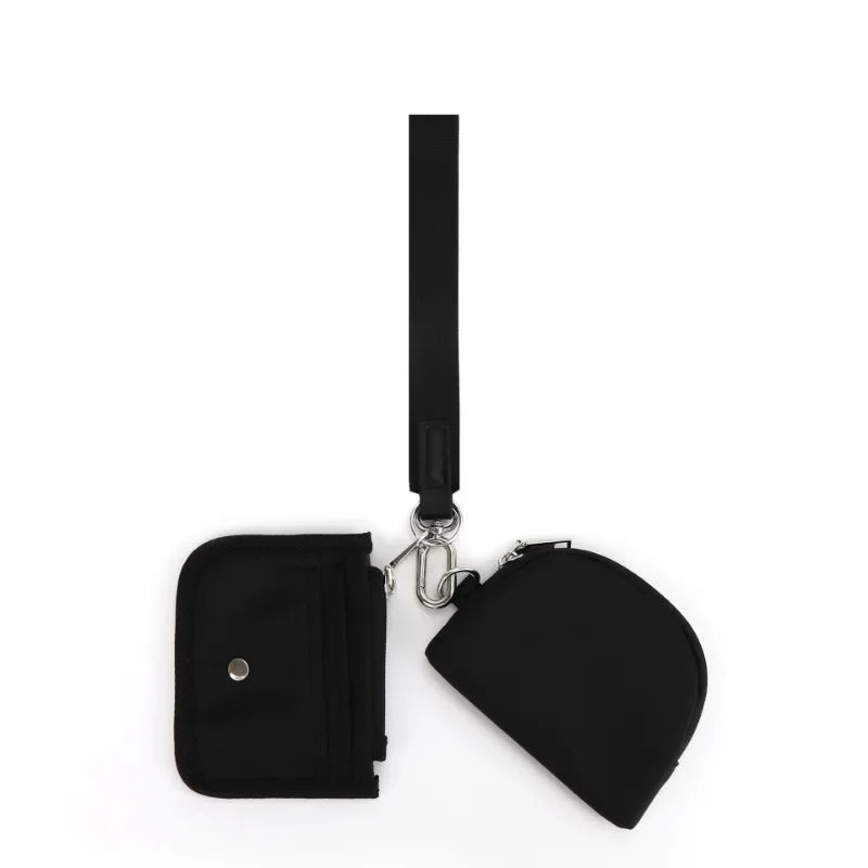 A black mini zip around wristlet wallet with a long strap is shown against a white background.