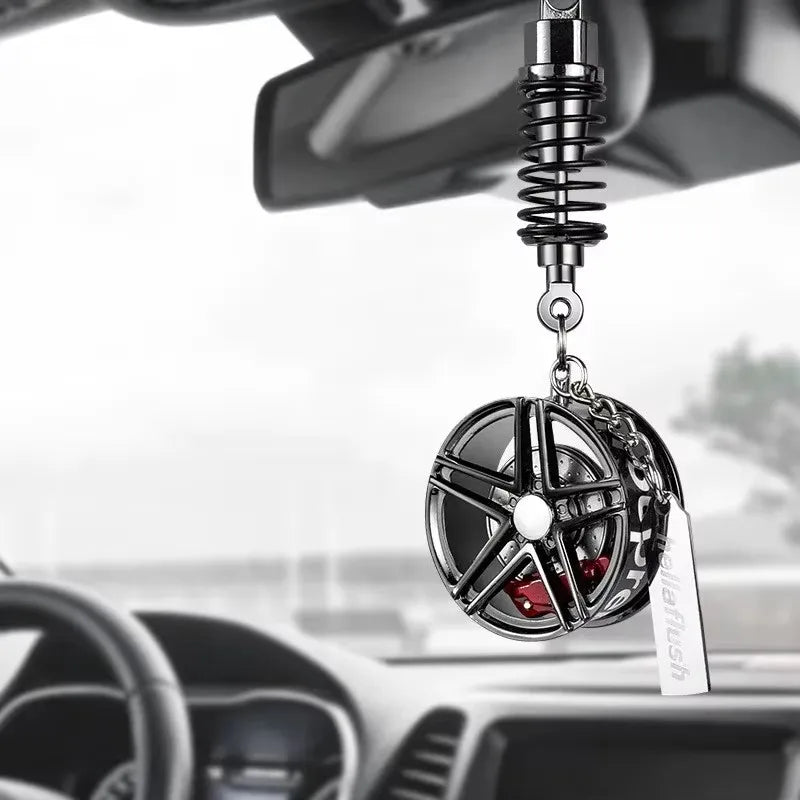 A black alloy wheel hub brake disc pendant hangs from a chain and is positioned in front of a car's rearview mirror.