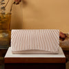 A beige satin evening clutch with vertical pleats rests on a wooden block against a warm brown background.