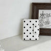A white polka dot passport holder with multi-card slots resting in front of a dark wooden framed picture.