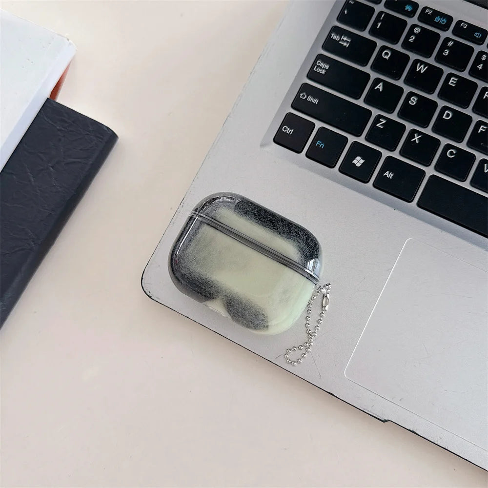 A clear, square-shaped earphone case with a luminous sand effect is resting on a silver laptop keyboard.