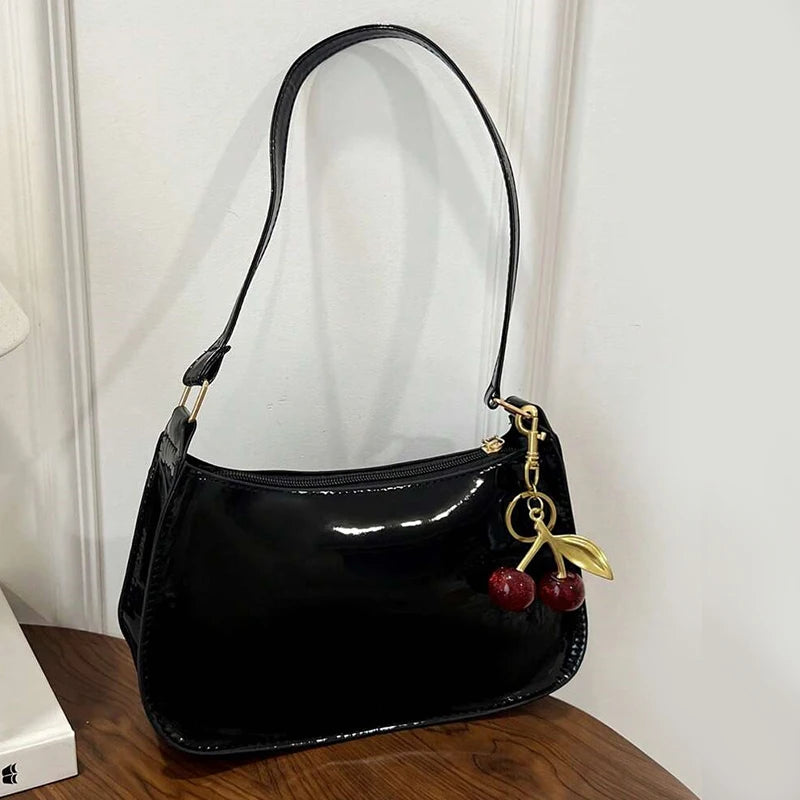 Black PU leather shoulder bag with a gold cherry pendant hanging from the strap.