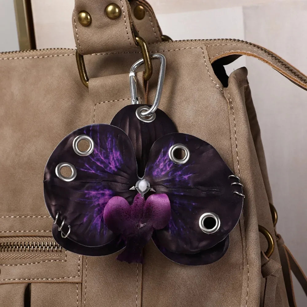 A dark purple orchid flower keychain attached to a tan leather handbag.