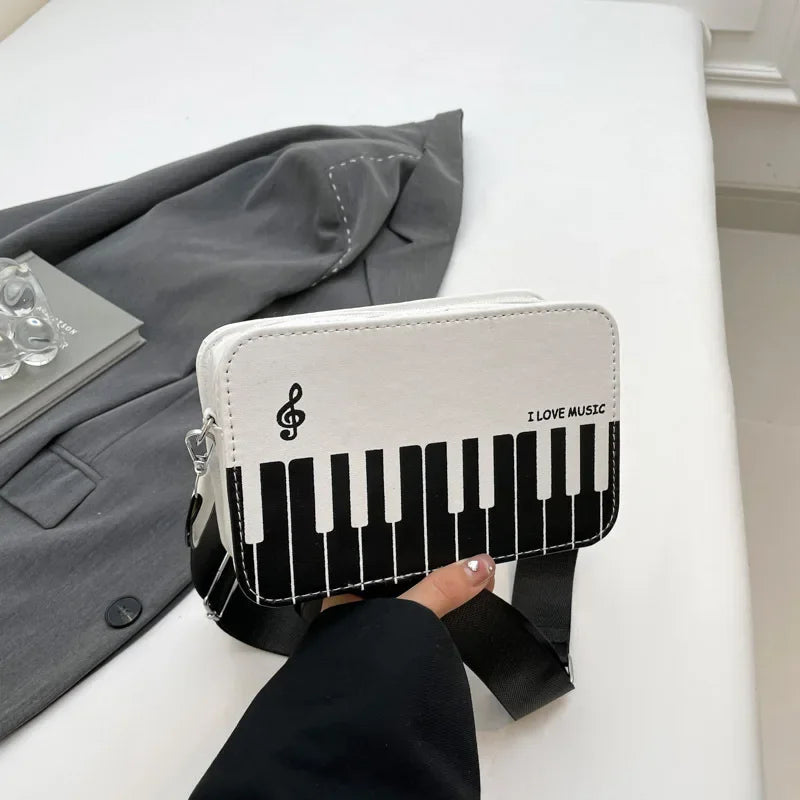 A white and black piano print crossbody bag with musical note embroidery resting on a white surface.