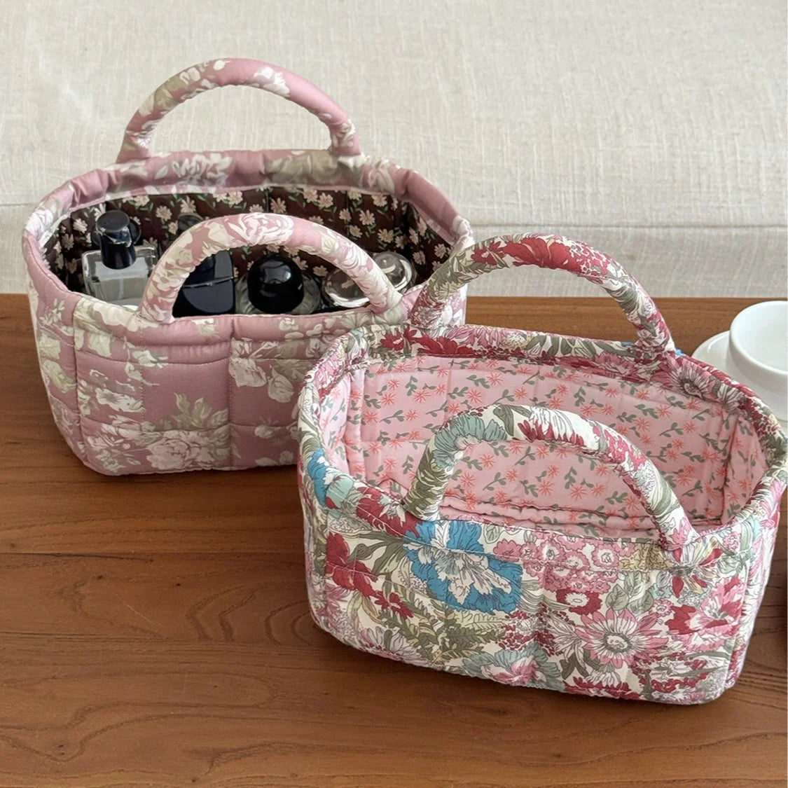 A pink quilted fabric storage basket with a floral pattern sits on a wooden surface.