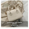 Sac à main en cuir PU beige clair minimaliste avec une poignée supérieure, à côté de téléphones mobiles.
