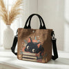 Braune Tasche mit Blumen-Katzenmuster und schwarzen Riemen, auf einer weißen Oberfläche.