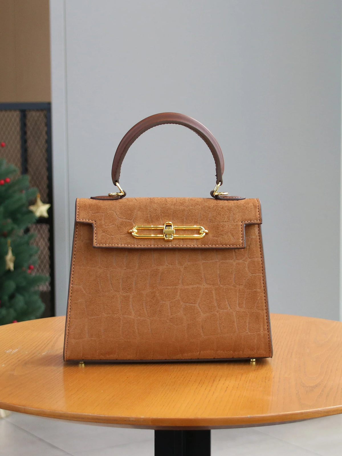 A tan leather tote bag with a crocodile pattern and gold hardware sitting on a wooden table.