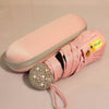A pink compact umbrella with a glittery rhinestone handle and UV protection label.