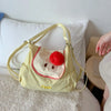 A light yellow nylon messenger backpack shaped like a face with a red nose and pink outline, resting on white bedding.