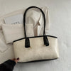 A beige leather tote bag with black trim and gold hardware resting on a white textured surface.