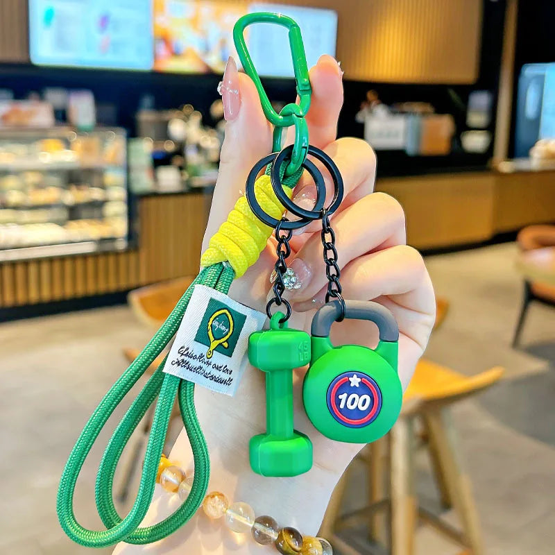 A hand holds a green nylon fitness keychain with a yellow strap and a green dumbbell charm.
