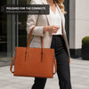 A woman carrying a large, tan leather laptop tote bag while walking outdoors.