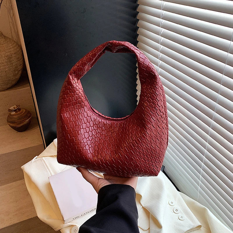 A close-up shot of a reddish-brown woven embossed hobo shoulder bag with a top handle being held against a white fabric backd