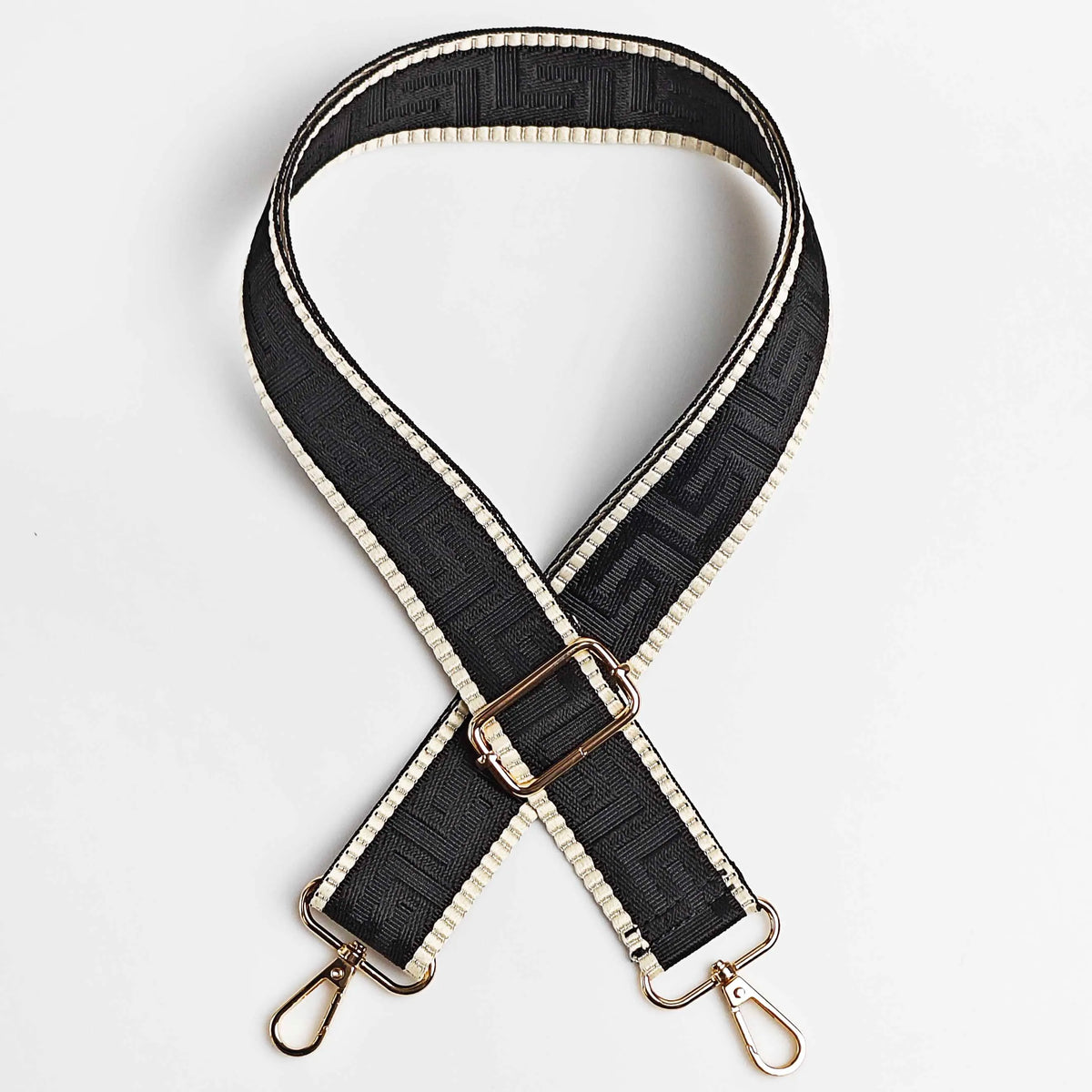 A black adjustable crossbody bag strap featuring a maze pattern and gold-toned hardware.