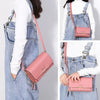 A woman wearing denim overalls and a white top, holding a pink multi-card shoulder wallet.